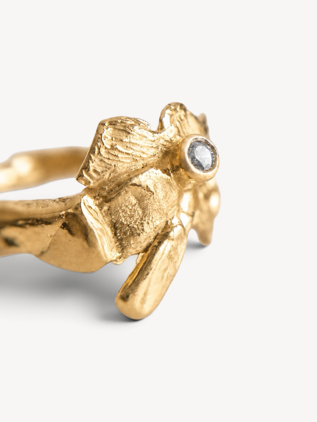 Close-up side view of a handcrafted 14k gold-plated sterling silver sculptural ring featuring a bezel-set white zircon and organic textured details.