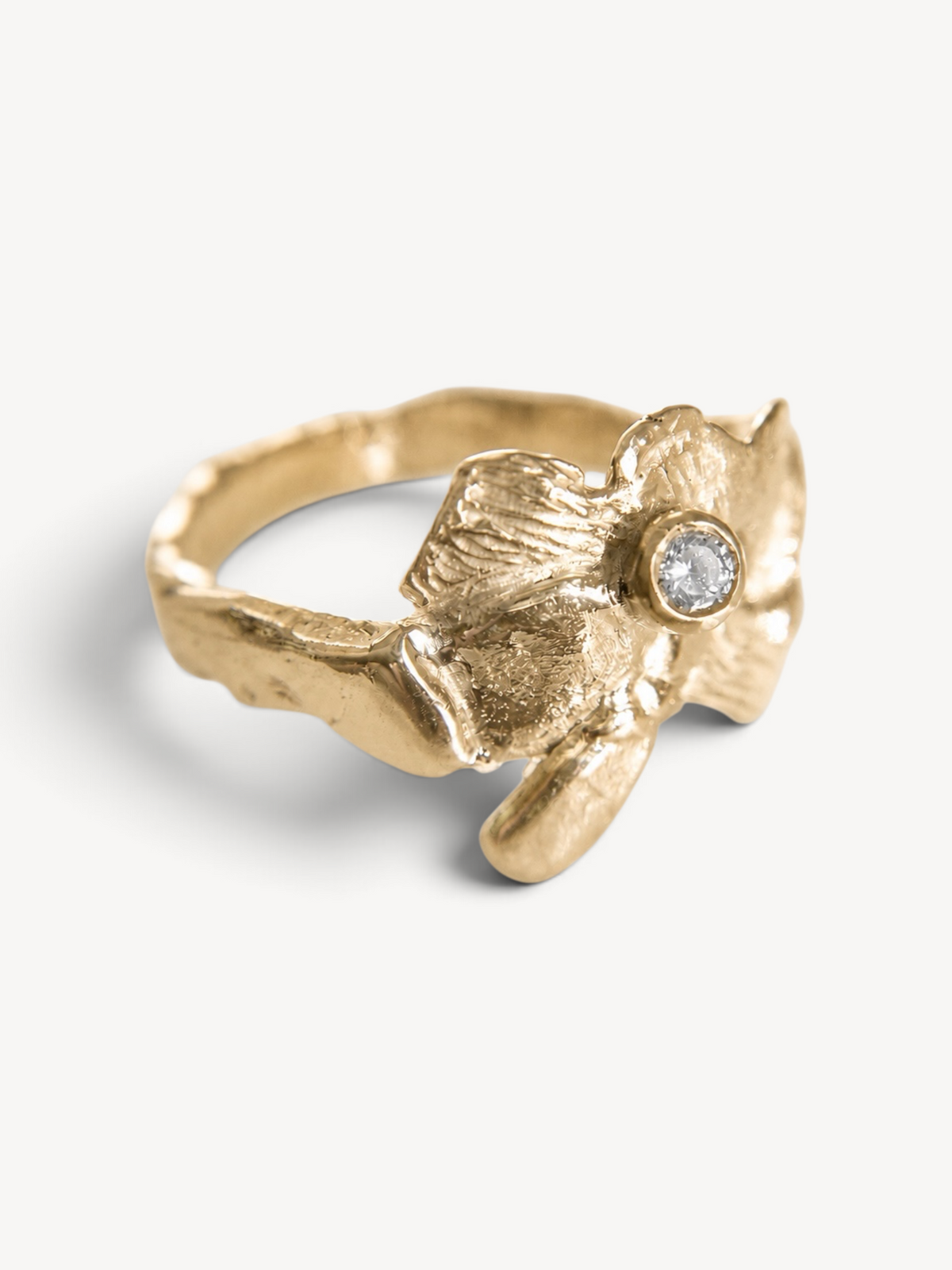 Three-quarter view of a handcrafted 14k gold-plated sterling silver statement ring with a bezel-set white zircon and organic floral design.