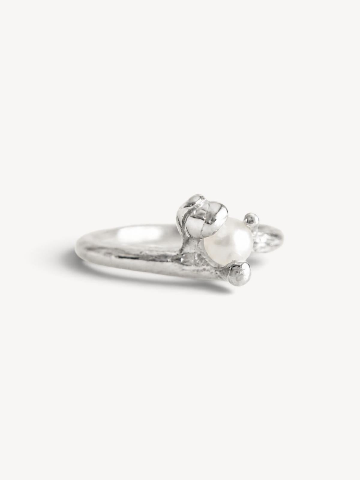 Angled front view of a handcrafted rhodium-plated sterling silver ring with a freshwater pearl in an organic sculptural setting.