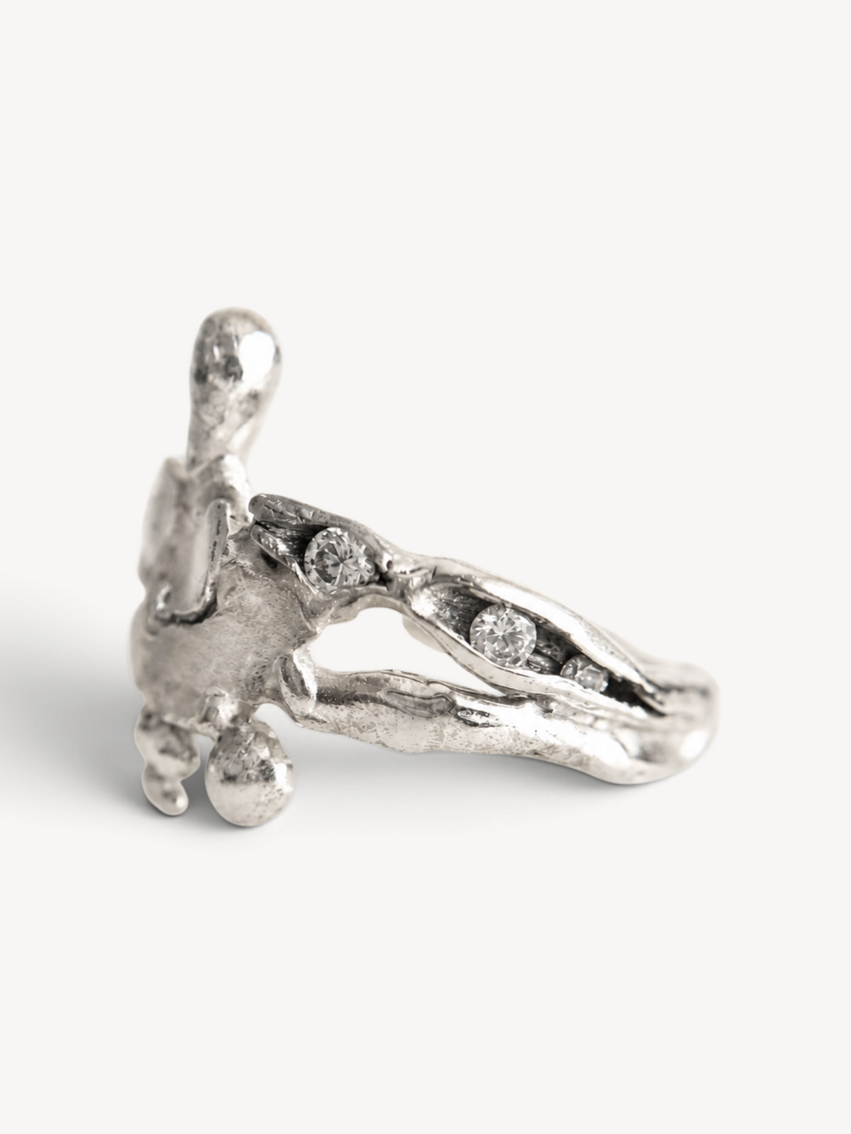 Side view of a handmade rhodium-plated sterling silver ring with an open sculptural design and three white zircon stones.