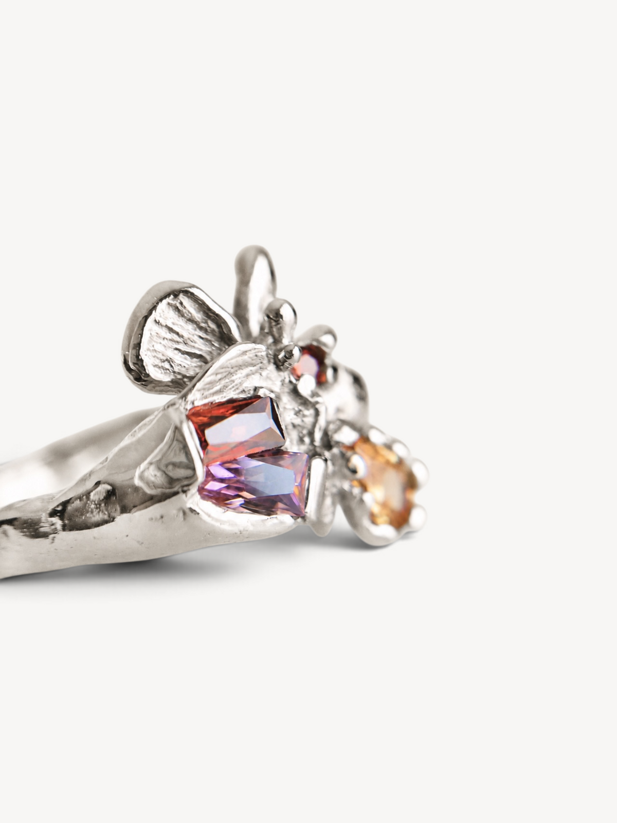 Side view of a contemporary rhodium-plated sterling silver ring with organic sculptural details and multicolor zircon stones.